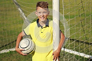 Boy football player in a yellow t-shirt stands near the goal with the ball