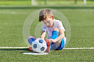 Boy football soccer tying laces him boots on grass