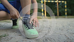 Boy footballer tying shoelaces, special orthopedic footwear for sportsman