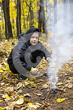 A boy in the forest is lighting a fire. Concept: lost in the forest, survival in the wild, lost without parents, a young traveler,