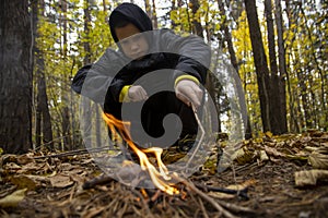 A boy in the forest is lighting a fire. Concept: lost in the forest, survival in the wild, lost without parents, a young traveler,