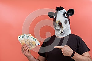 Boy with funny latex cow mask holding money with one hand and pointing to it with the finger of the other hand