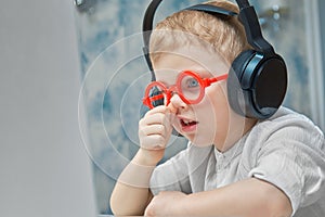 A boy in funny red glasses goes through online training on a laptop and picks his nose out of boredom