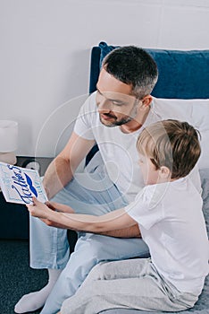 Boy gifting handmade fathers day greeting card to happy father