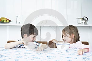 Boy and girl (5-6) sitting at table eating cereal and looking in eyes