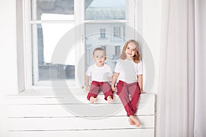 Boy and girl are brother and sister sit on the windowsill at the window