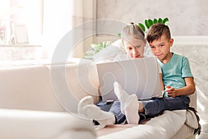 Boy and girl, brother and sister watching a video together on a laptop while sitting on a sofa at home