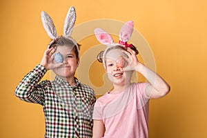 A boy with a girl with bunny ears hold Easter eggs in his hands