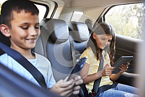 Boy and girl in a car using tablets during family road trip