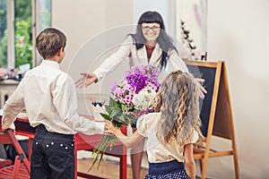 Boy and girl children give flowers as a school teacher in teache