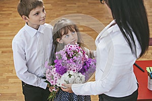 Boy and girl children give flowers as a school teacher