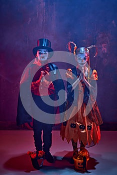 Boy and girl, children in halloween costumes, standing with basket for candies and betting for treat against dark