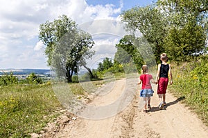 A boy and a girl children walk on a dirt road on a sunny summer day. Kids holding hands together while enjoying ativity outdoors.
