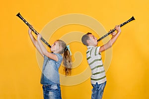 A boy and a girl with clarinets are standing with their backs to each other, playing the clarinet, on a yellow background