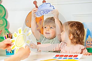 Boy, girl in the class play with weather rain and sun cards