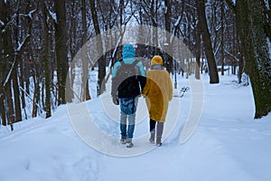 Boy and girl couple relationship walking back to camera in winter park in snowfall weather