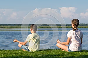 Boy and girl doing yoga outdoors by the lake