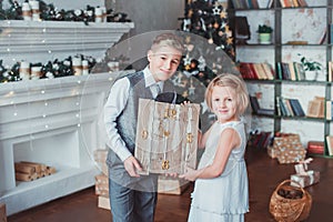 Boy and girl dressed elegantly standing in a bright room by the fireplace. Christmas tree in the background