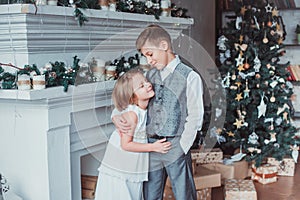 Boy and girl dressed elegantly standing in a bright room by the fireplace. Christmas tree in the background. New year concept