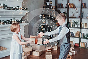 Boy and girl dressed elegantly standing in a bright room by the fireplace. Christmas tree in the background. New year concept.