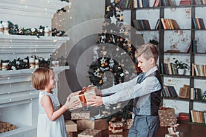Boy and girl dressed elegantly standing in a bright room by the fireplace. Christmas tree in the background. New year concept.