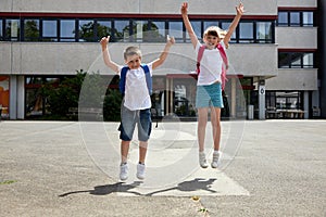 A boy and a girl happily jump up near the school. Joy at the beginning of the school year or the end of lessons. Children are