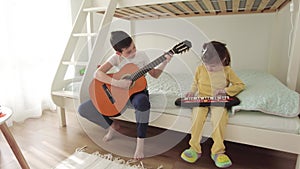 Boy and girl having fun together playing music at home. Brother plays the guitar, the sister the keyboard.