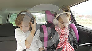 Boy and Girl with Headphones Playing a Tablet and smartphone in a Car, Children Using a Devices in the auto. Brother and