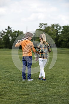 Boy and girl holding hands while standing on green field, boy holding badminton racquet on his shoulder