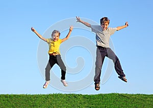 Boy and girl jump together at grass