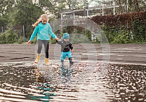 Boy and girl jumping in puddle in waterproof coat and rubber boots