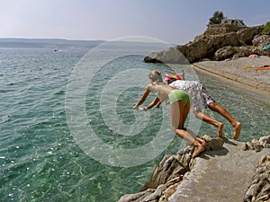 Boy and girl jumping into the sea from the rocks