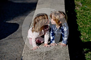 Boy and girl kiss on stone kerb on sunny day