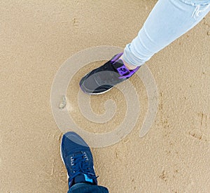 Boy and girl legss, sports shoes and sea-shell on sand