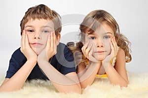 Boy and girl lying on white fell, chin on hands photo