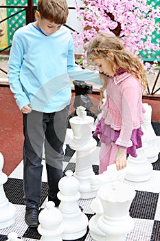 Boy and girl move big chess pieces on big chessboard
