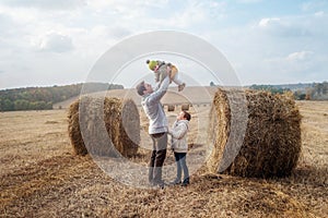 A boy and a girl near a haystack in a field at sun day on autumn next to a tractor cleans field