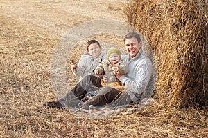 A boy and a girl near a haystack in a field at sun day on autumn next to a tractor cleans field