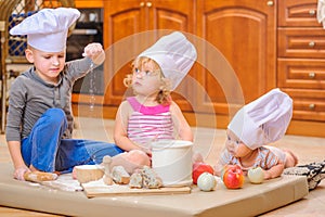 Boy and girl and a newborn kid with them in chef`s hats sitting on the kitchen floor soiled with flour photo