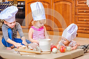 Boy and girl and a newborn kid with them in chef`s hats sitting on the kitchen floor soiled with flour photo