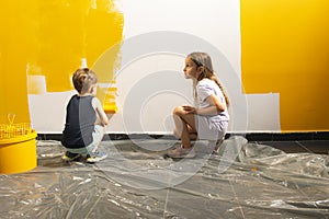 A boy and a girl paints a wall at home in yellow