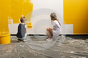 A boy and a girl paints a wall at home in yellow