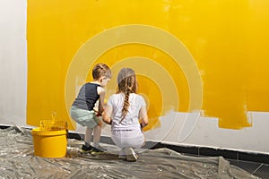 A boy and a girl paints a wall at home in yellow