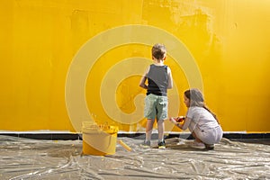 A boy and a girl paints a wall at home in yellow