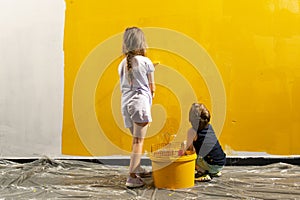 A boy and a girl paints a wall at home in yellow