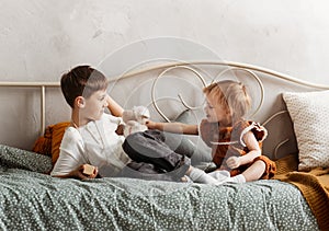 Boy and girl play on the bed in the children`s bedroom. Brother and sister happily spend time together