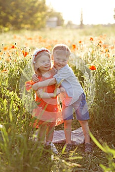 Boy with a girl play in a poppy field, children`s happiness