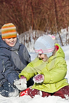 Boy and girl play sitting in snow in winter