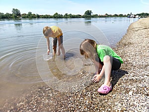 A boy and a girl are playing on the beach. Children play with water, sand and pebbles on the river bank.