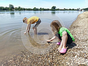 A boy and a girl are playing on the beach. Children play with water, sand and pebbles on the river bank.